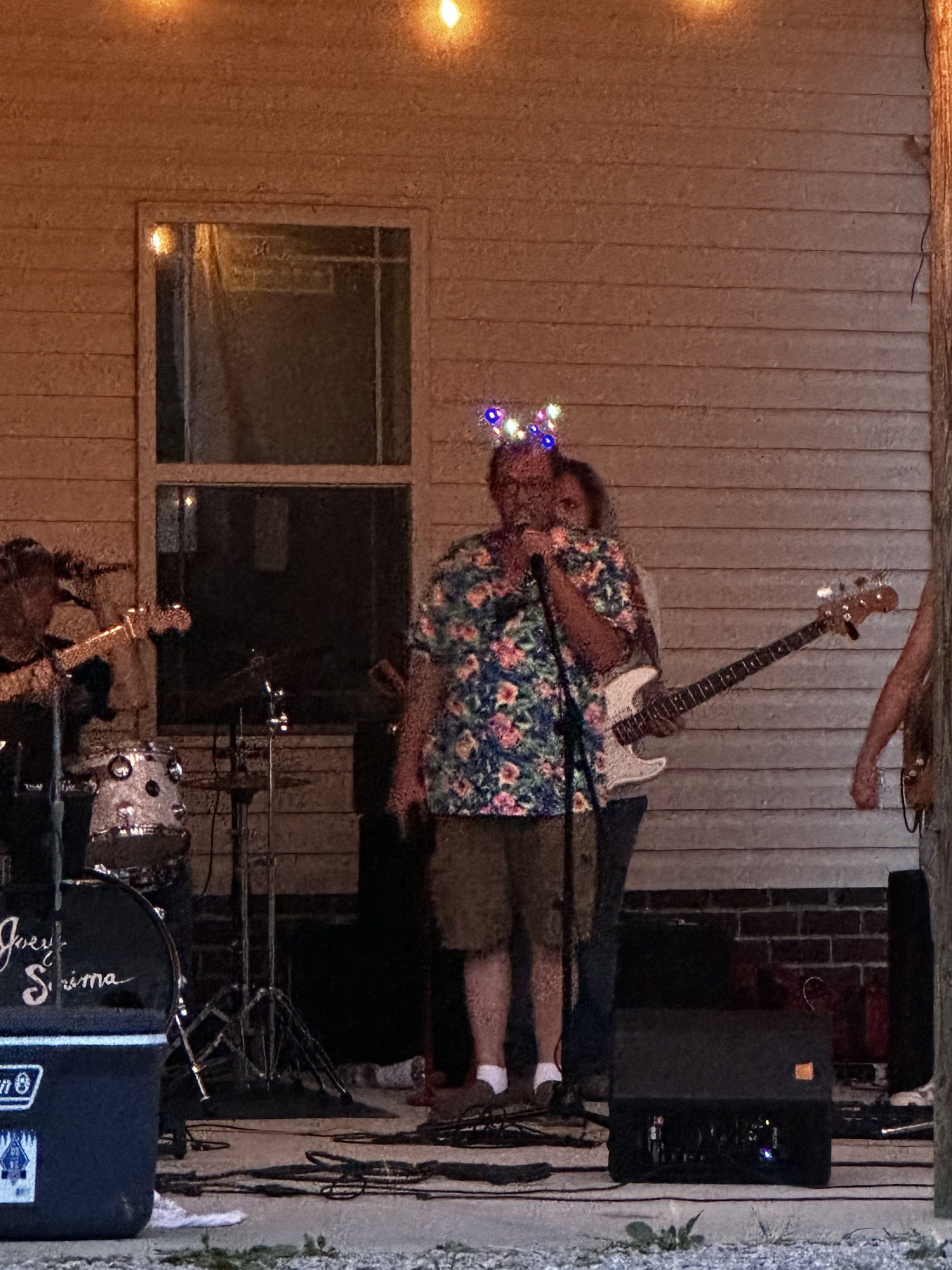 The band performing on the porch at night under string lights, with Kevin at the microphone